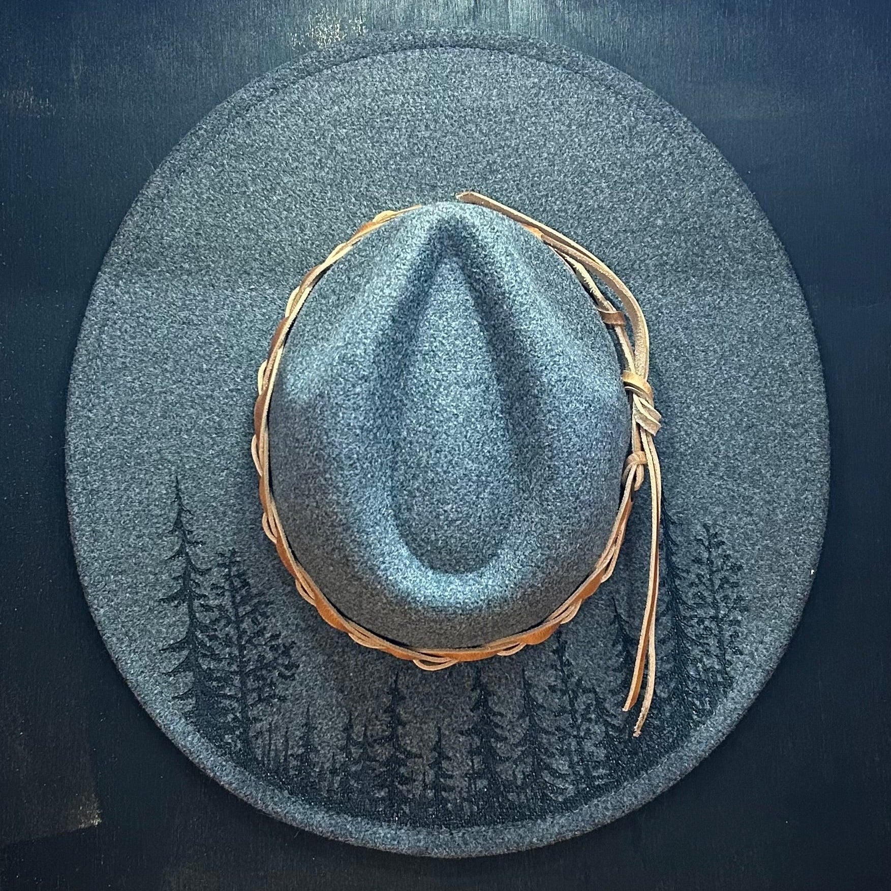 Moody, high-contrast tree silhouette hand-burned with a charcoal-sketch texture on a premium felt hat. Deep scorched-earth mountain art.