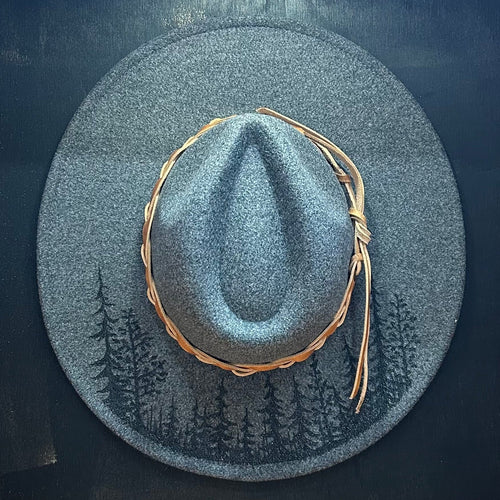 Moody, high-contrast tree silhouette hand-burned with a charcoal-sketch texture on a premium felt hat. Deep scorched-earth mountain art.