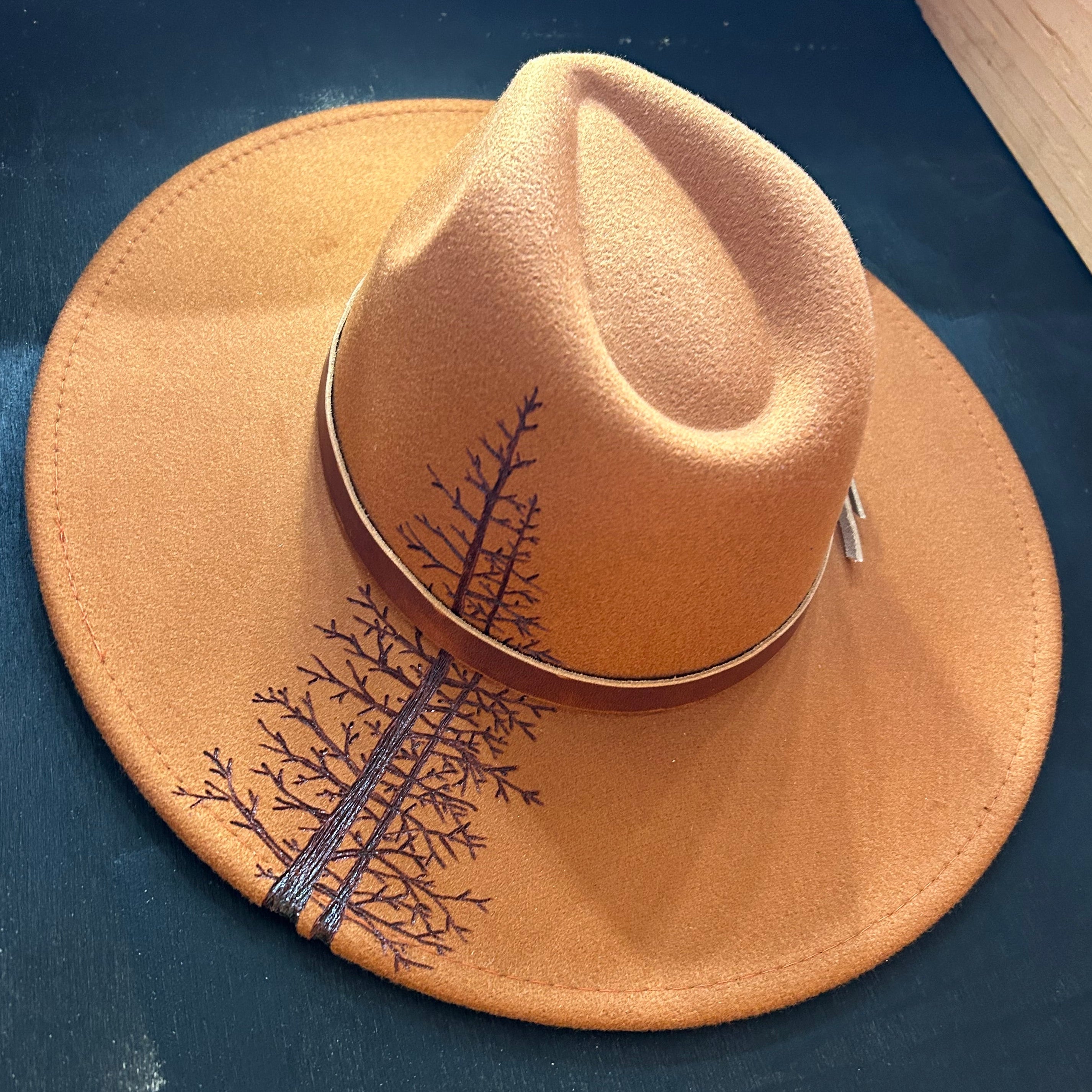 Fine-line etching of tamarack needles and skeletal larch branches hand-burned into a bone-colored felt hat. A moody tribute to the autumn transition in the high country.