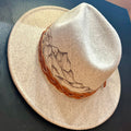 Hand-burned mountain landscape etching along the crown of a custom felt hat. A jagged, minimalist peak silhouette designed for high-altitude style.