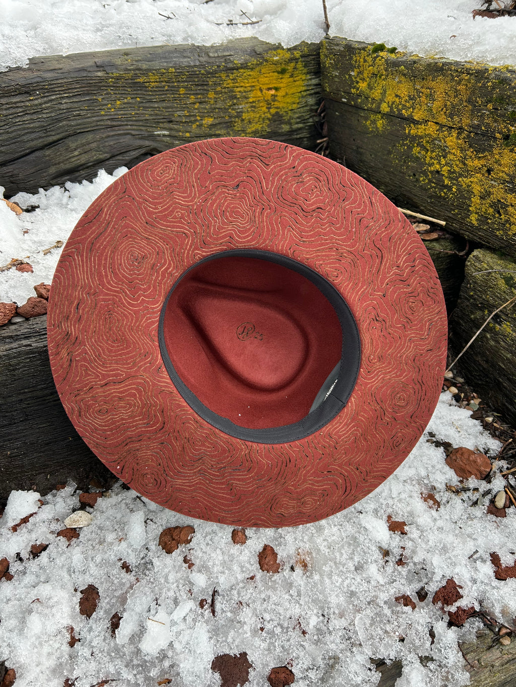 A hand-burned combination of topographic map contour lines and a timberline forest silhouette on a custom felt hat. Artistic mapping and tree pyrography by Hleritz Customs.
