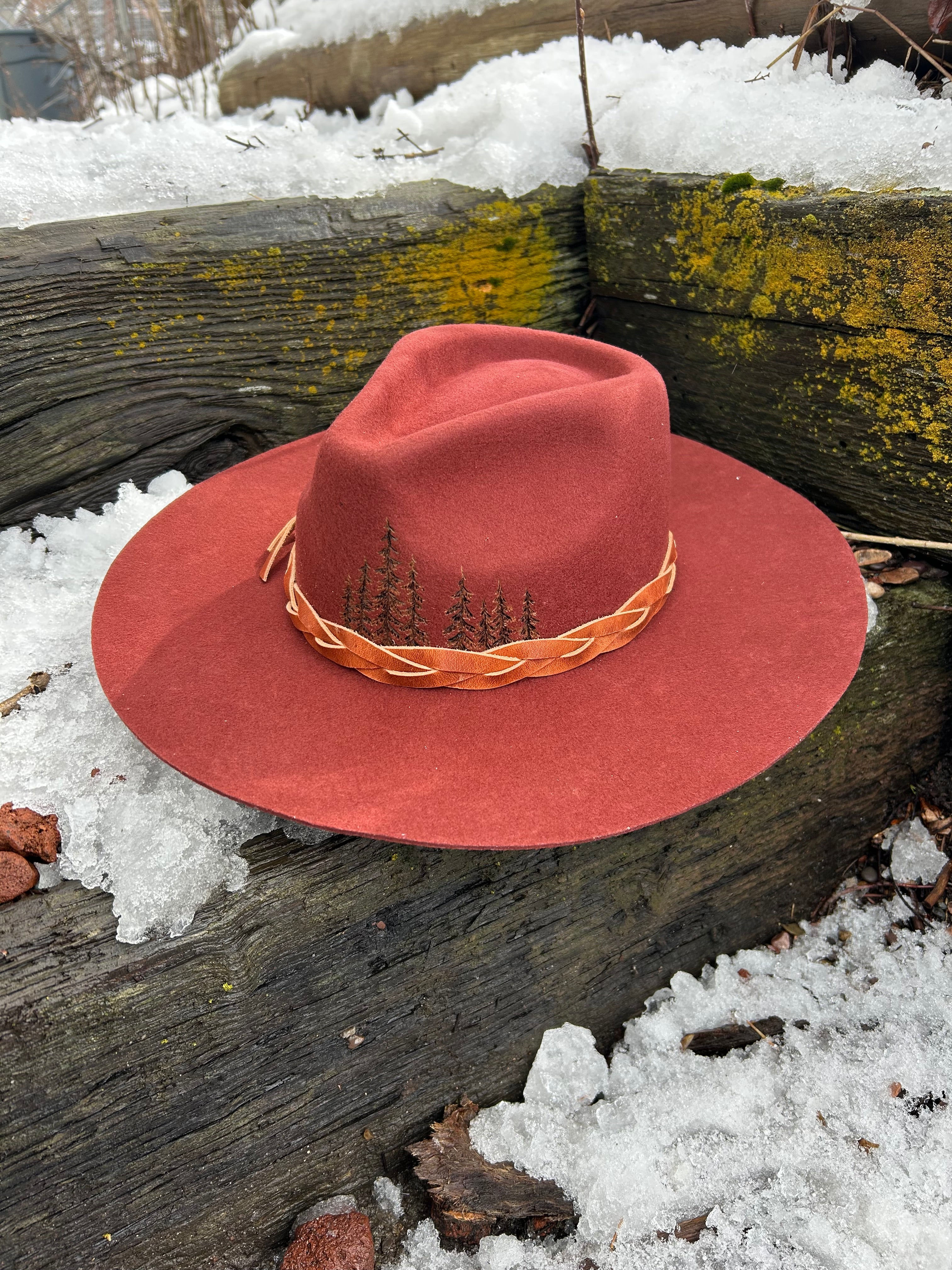 A hand-burned combination of topographic map contour lines and a timberline forest silhouette on the crown of a felt hat. Artistic mapping and tree pyrography by Hleritz Customs.