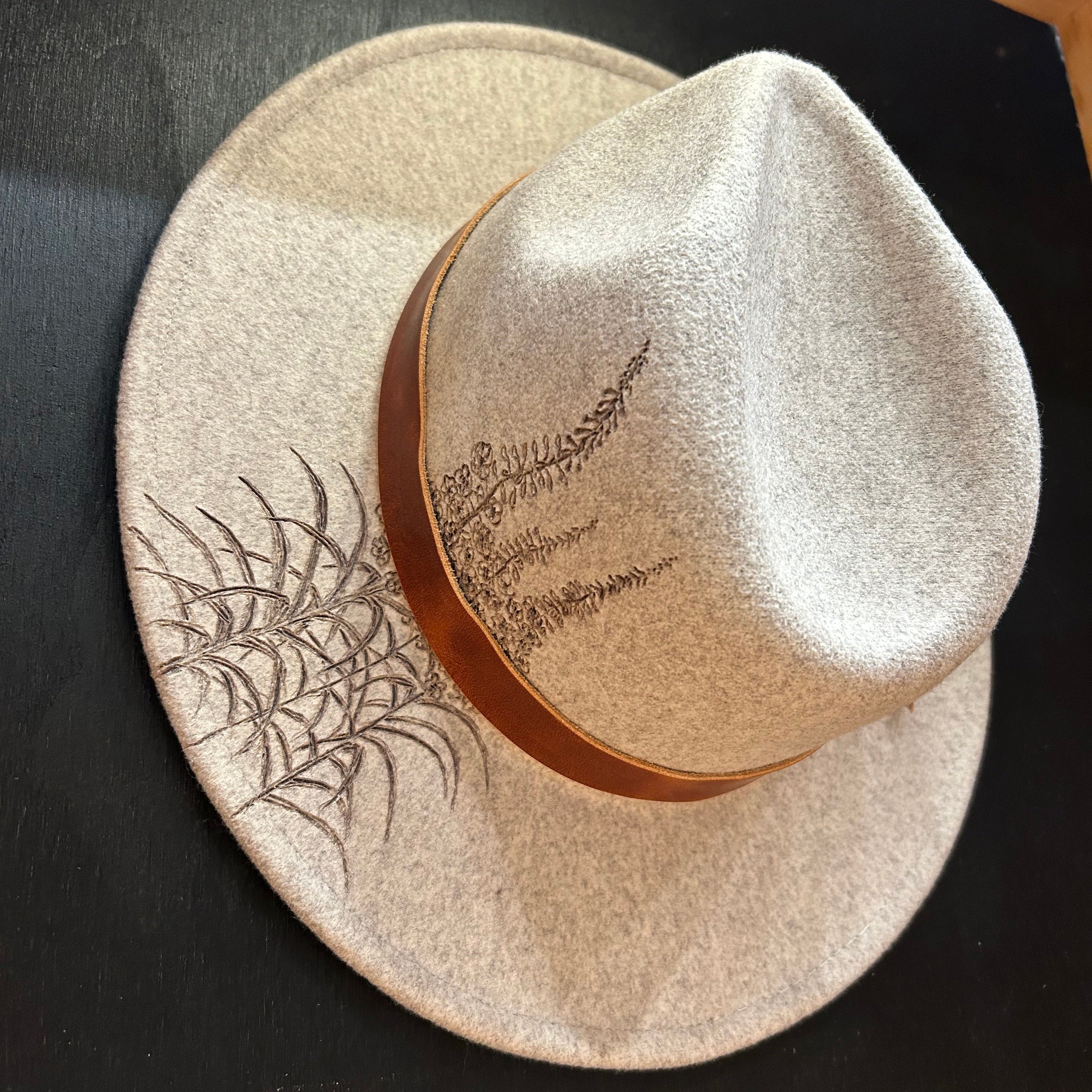 Detailed hand-etched fireweed stalks and floral silhouettes on a custom structured hat. Artistic scorched-earth botanical design celebrating resilience and mountain summer blooms.