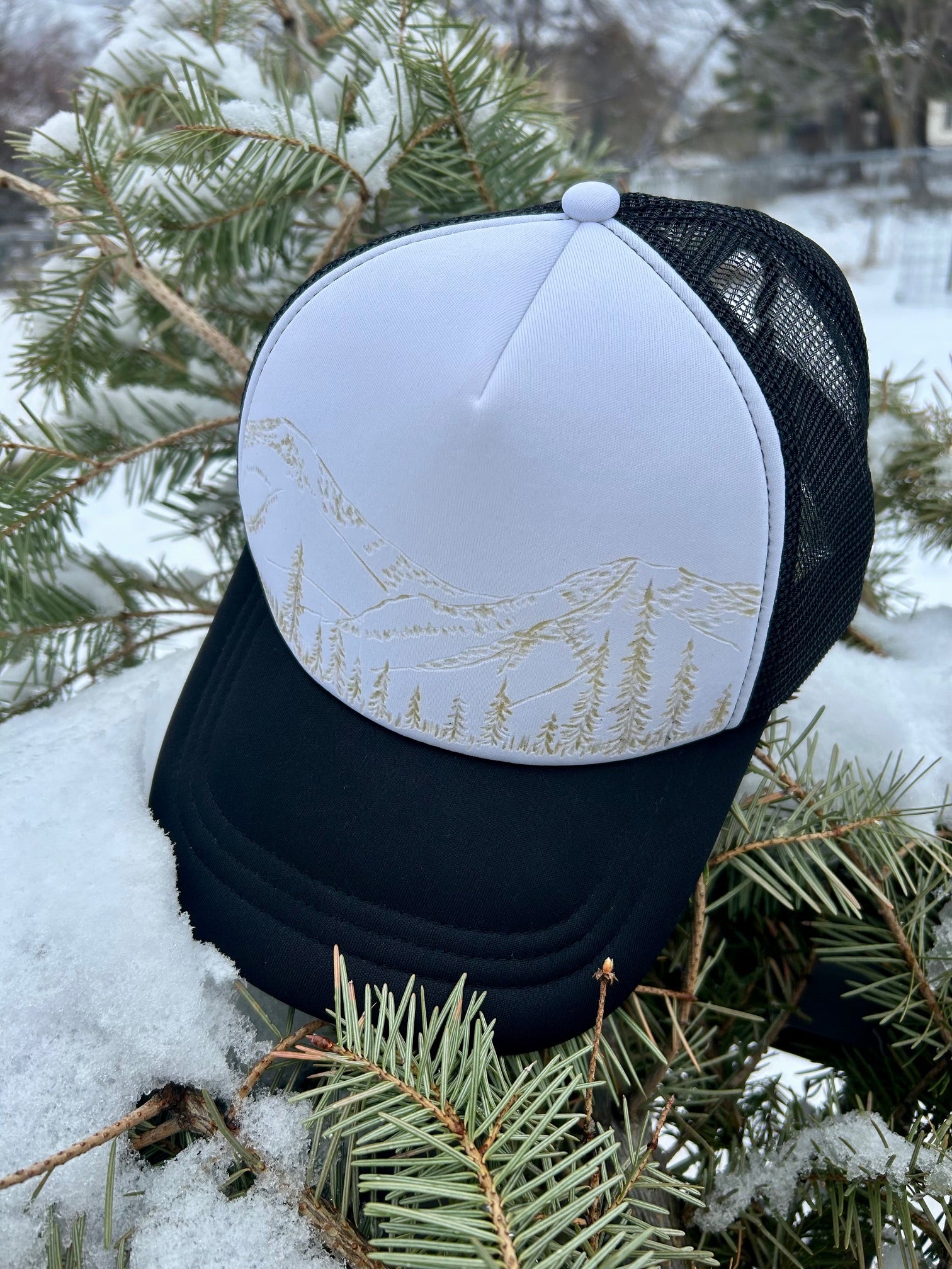 Close-up of the Wilderness Trucker hat: raw, fire-carved nature art on a crisp white panel.
