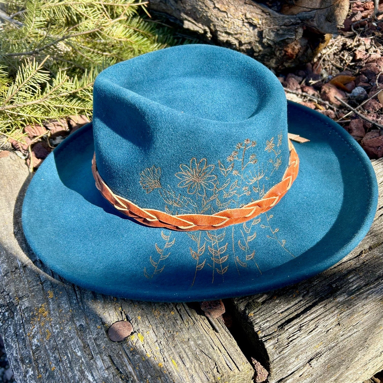 An intricate and chaotic hand-etched floral design flowing from brim to crown of a premium felt hat.