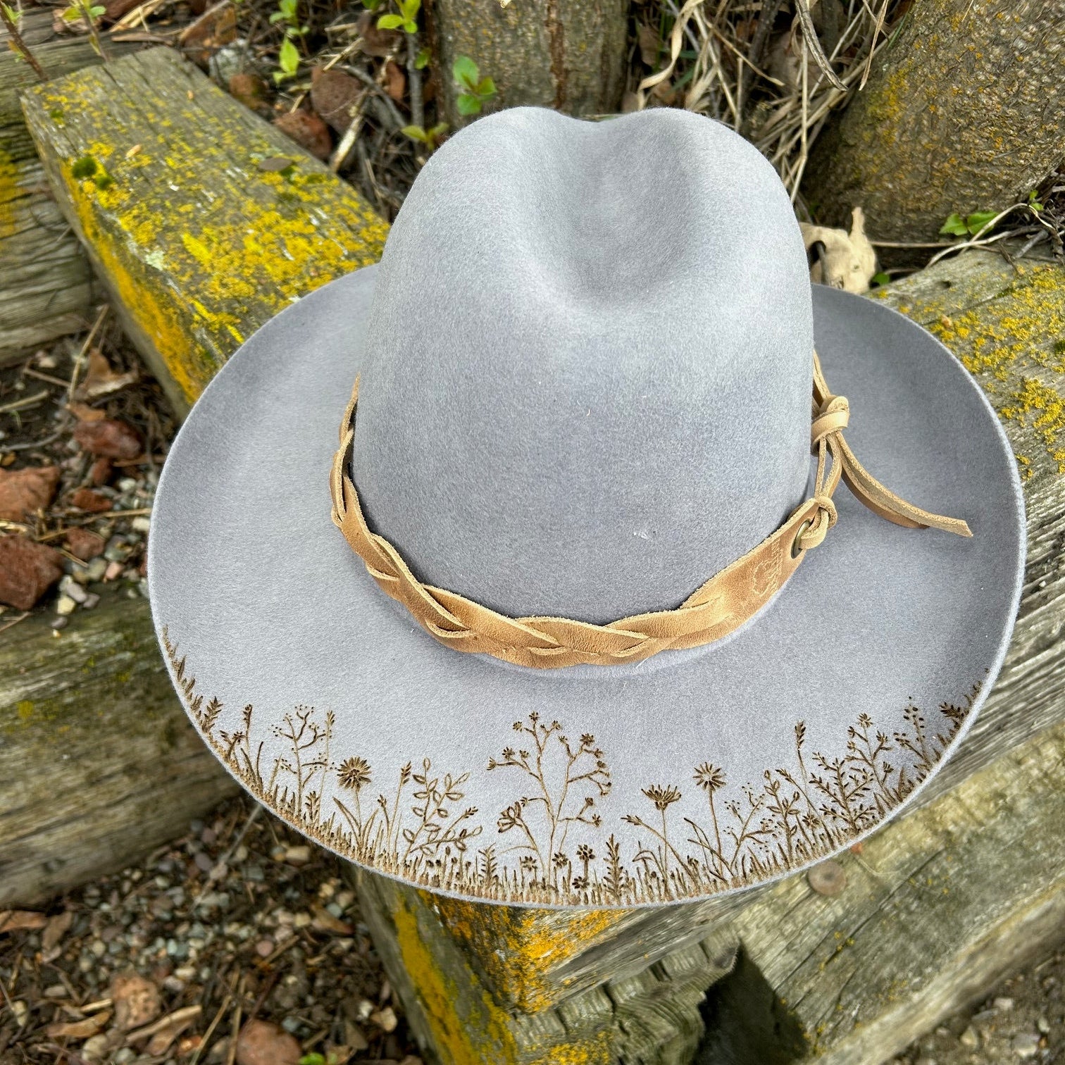 Hand-etched wildflower pyrography on the brim of a gray wool hat with a tan leather accent.